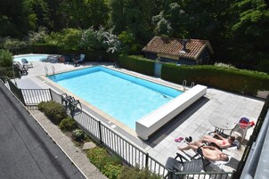 Una piscina rectangular con solárium de azulejos, rodeada por una valla metálica. Se observan sillas de descanso y una mesita con mantel.