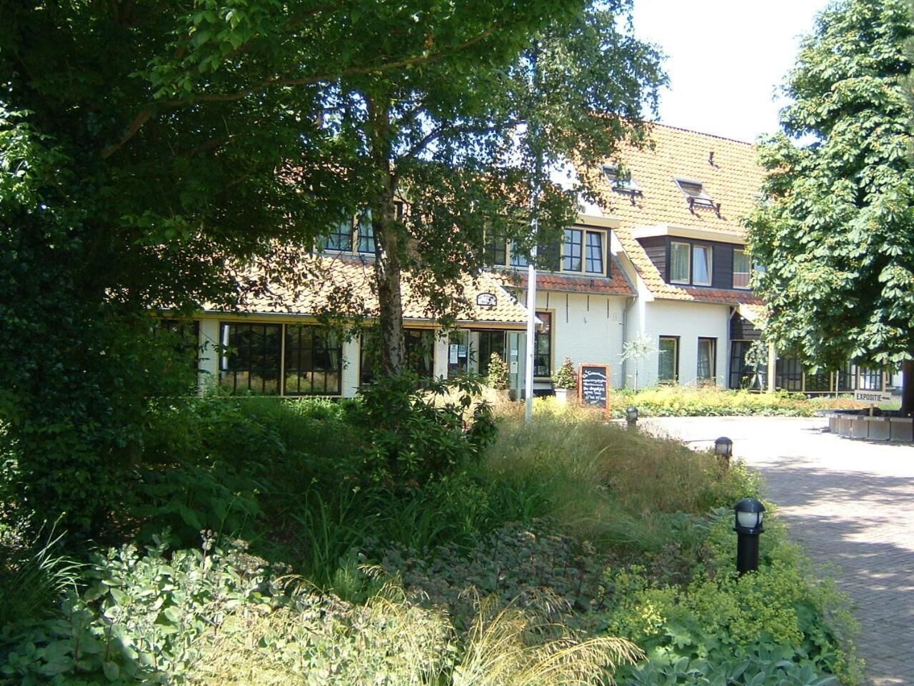 Een gebouw in traditionele bouwstijl, omgeven door weelderig groen en een verhard pad.