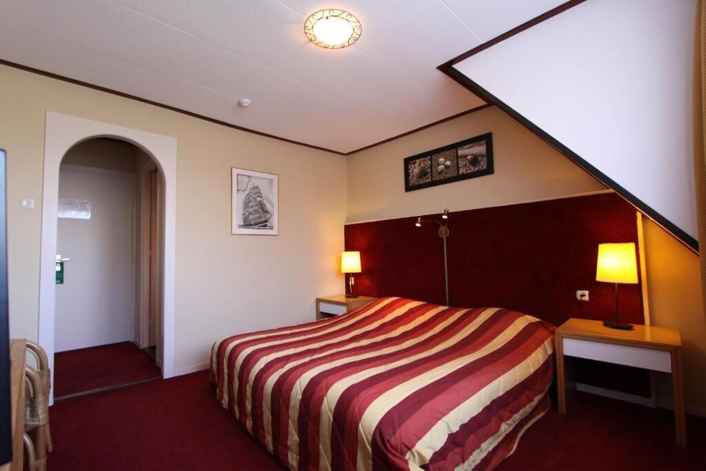 A hotel room with a bed, two bedside tables, a nightstand, a door, and a wall-mounted artwork.