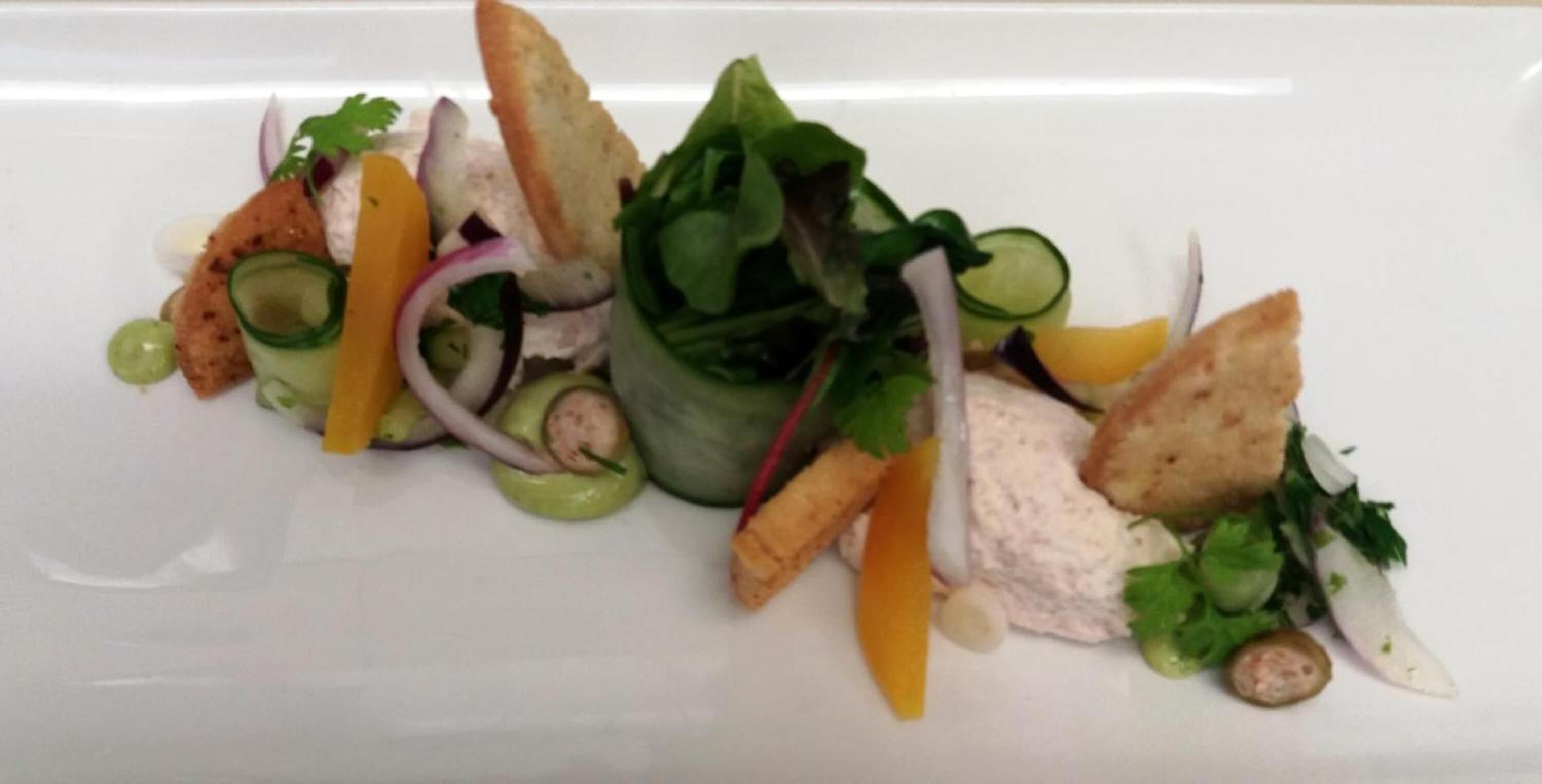 A white plate with a variety of food items including greens, slices of orange, and bread pieces.