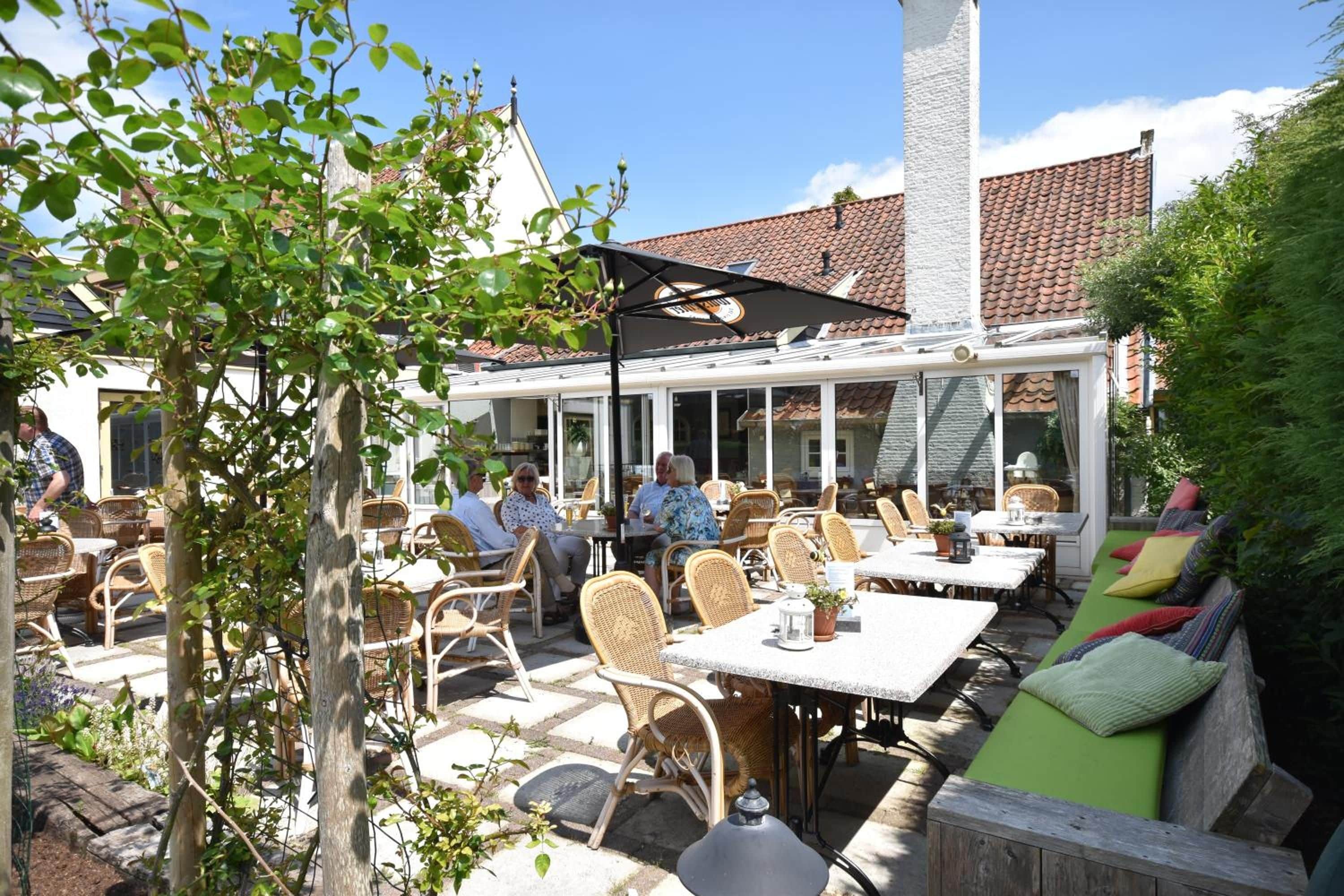 An outdoor patio area with tables and chairs, a covered seating area, and a building with a tiled roof in the background.