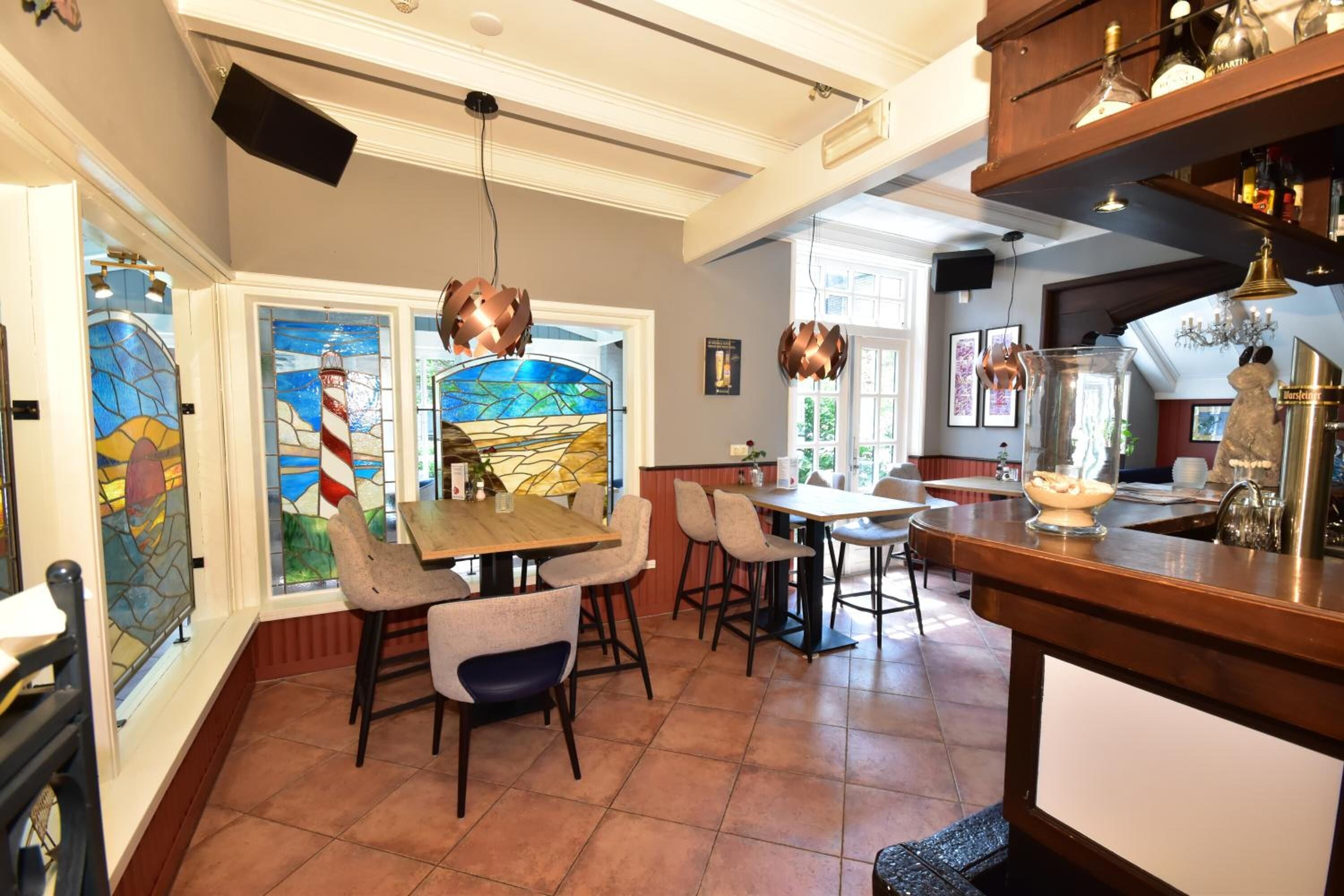Un área de comedor con una mesa grande y sillas, una barra y una ventana de vidrio emplomado con un diseño de faro.