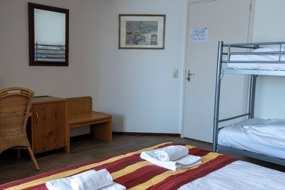 Une chambre d’hôtel avec des lits superposés, un bureau, une chaise et un lit recouvert d’une couverture à rayures.