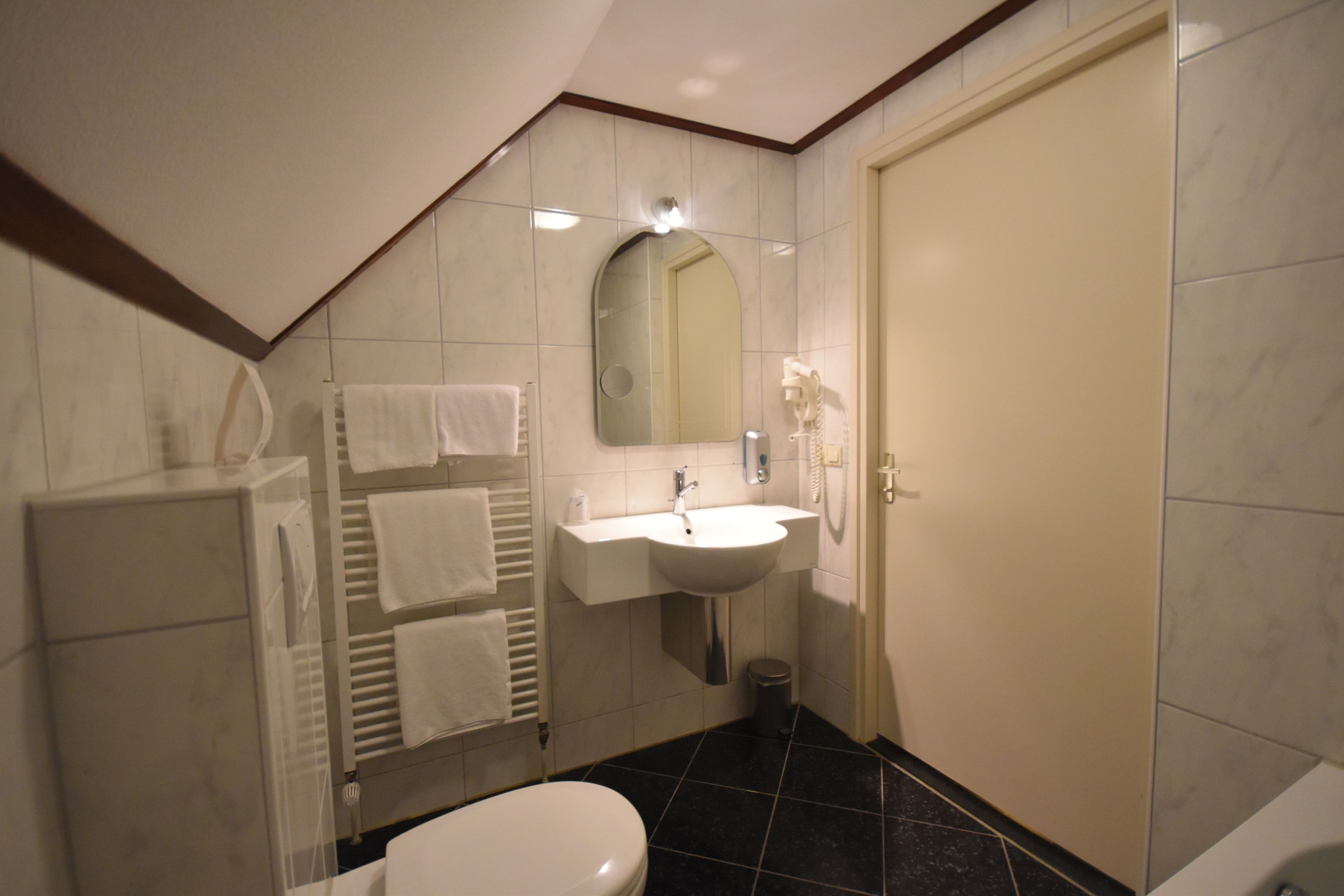 A bathroom with a toilet, sink, mirror, towel rack, and a door.