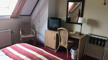 Une chambre d’hôtel avec un lit, un bureau avec un ordinateur, une chaise, un radiateur, une fenêtre avec des rideaux et un miroir au mur.
