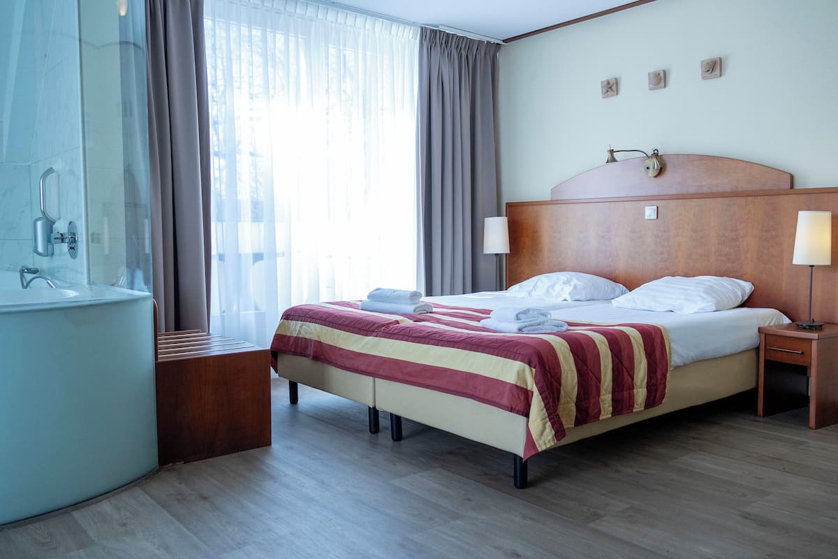 Une chambre d’hôtel comprenant un lit, une table de chevet, une lampe et une salle de bain avec un lavabo et une douche.
