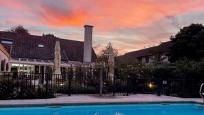 Une piscine avec vue sur le coucher de soleil, un patio couvert et un bâtiment en briques doté d’une cheminée.