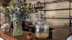 Un espace bar avec un comptoir en bois, des bocaux en verre et un vase rempli de fleurs.