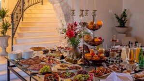 A breakfast buffet with various food items, a vase of flowers, and a staircase in the background. - Puteus Palace Brac (Pucisca)