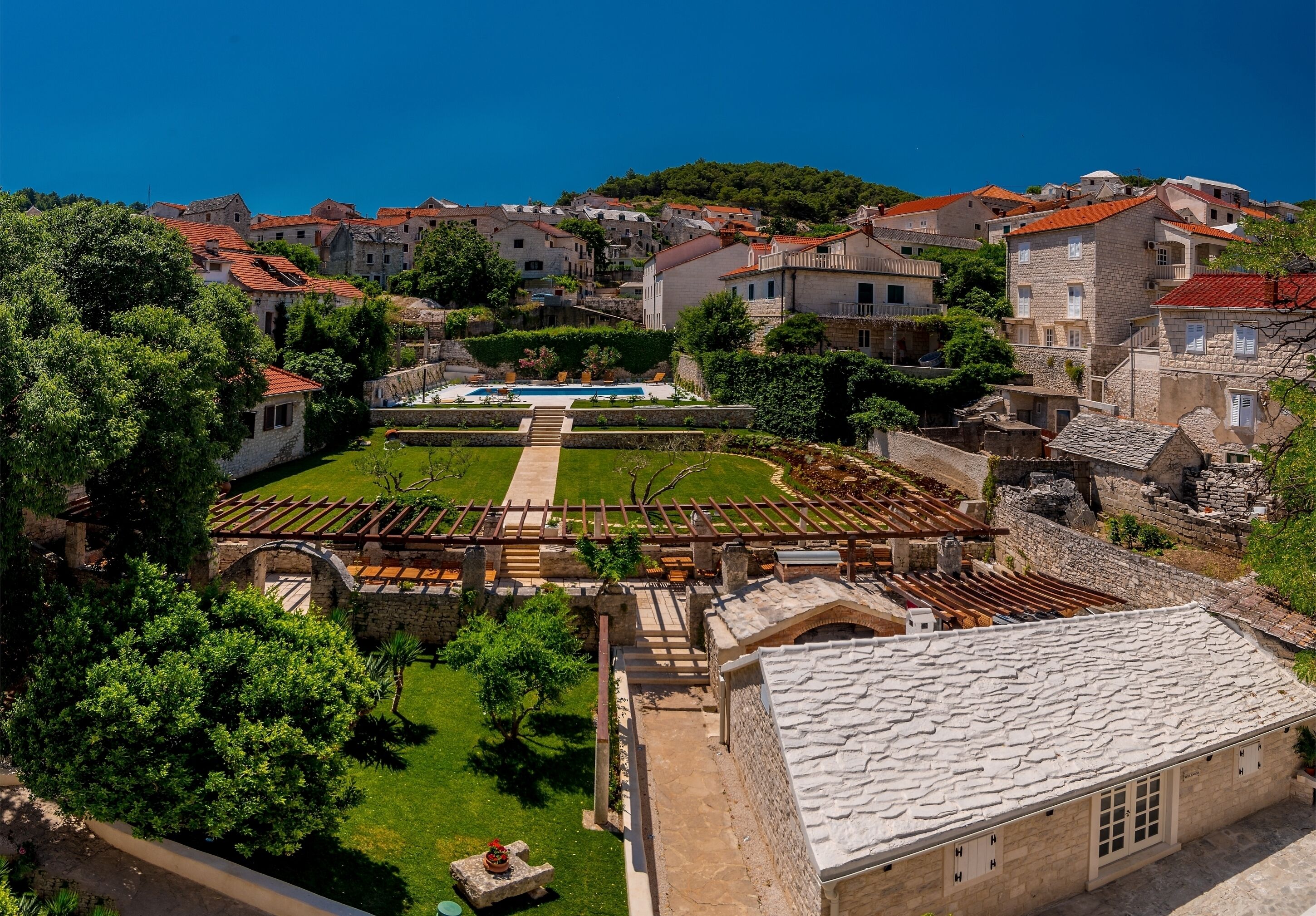A historic town with stone buildings, a central courtyard with a pool, and a hillside backdrop.