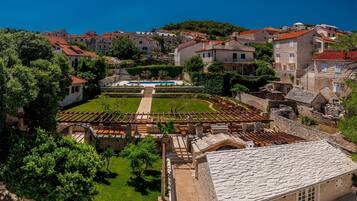A historic town with stone buildings, a central courtyard with a pool, and a hillside backdrop.