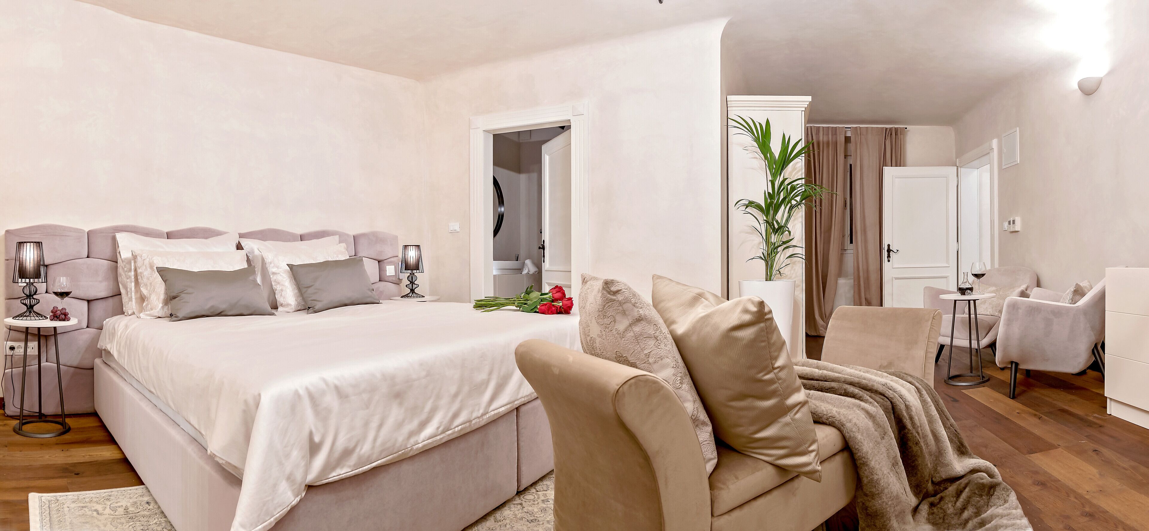 A bedroom with a bed, bedside tables, a chair, a plant, and a mirror.