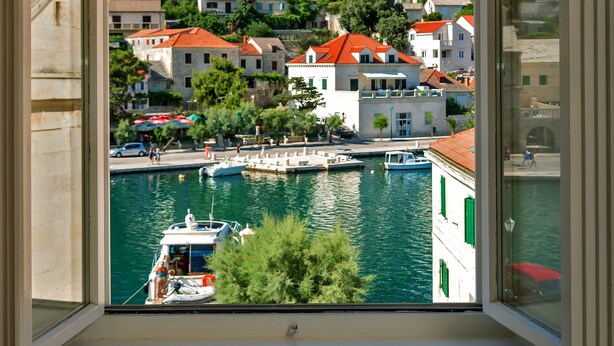 A view from a window overlooking a coastal town with buildings, a marina, and a clear blue sky. - Puteus Palace Brac (Pucisca)