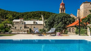 A swimming pool with lounge chairs, a stone building, and a tower in the background. - Puteus Palace Brac (Pucisca)