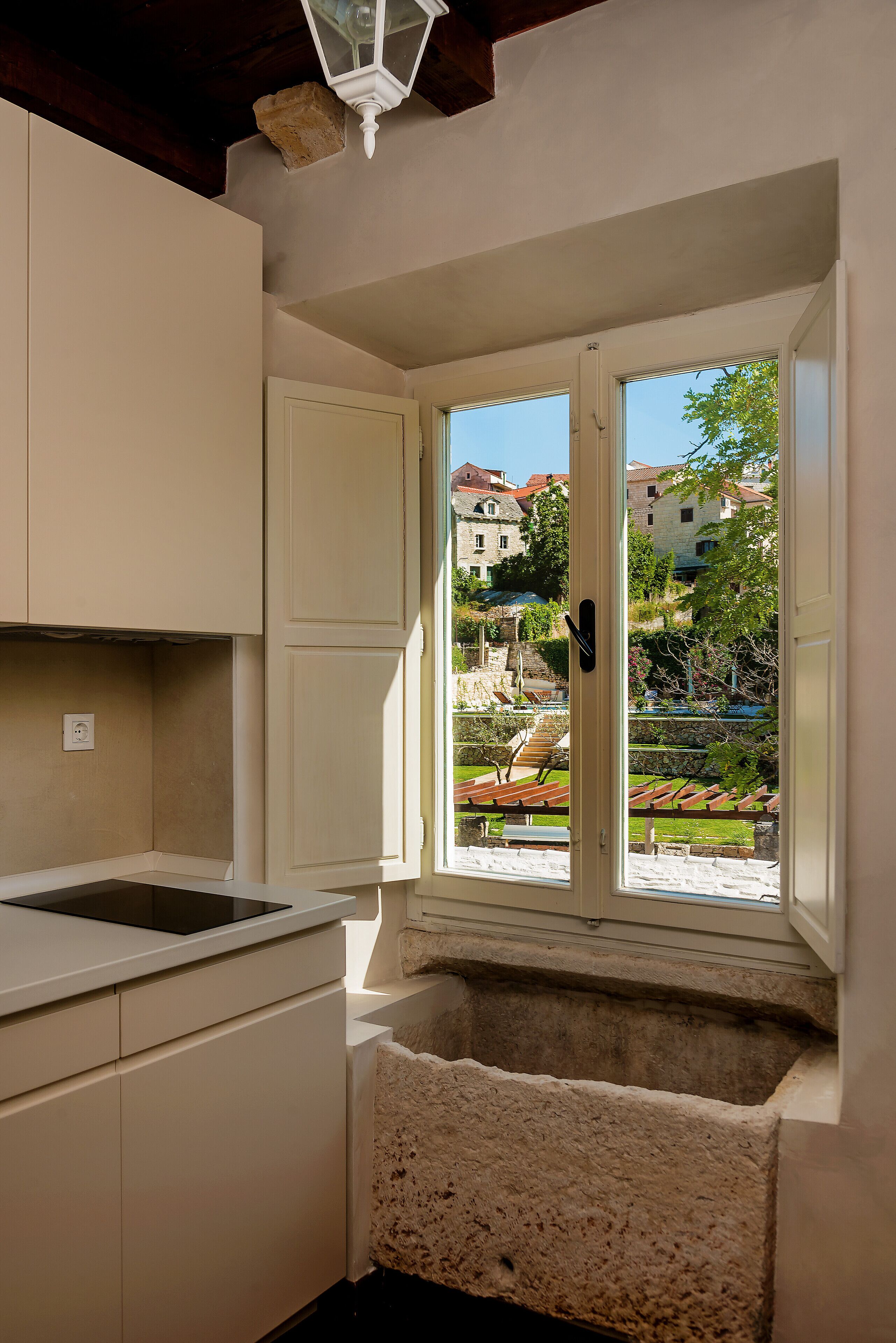 Una cocina con ventana, un lavamanos de piedra y vistas a edificios y vegetación.