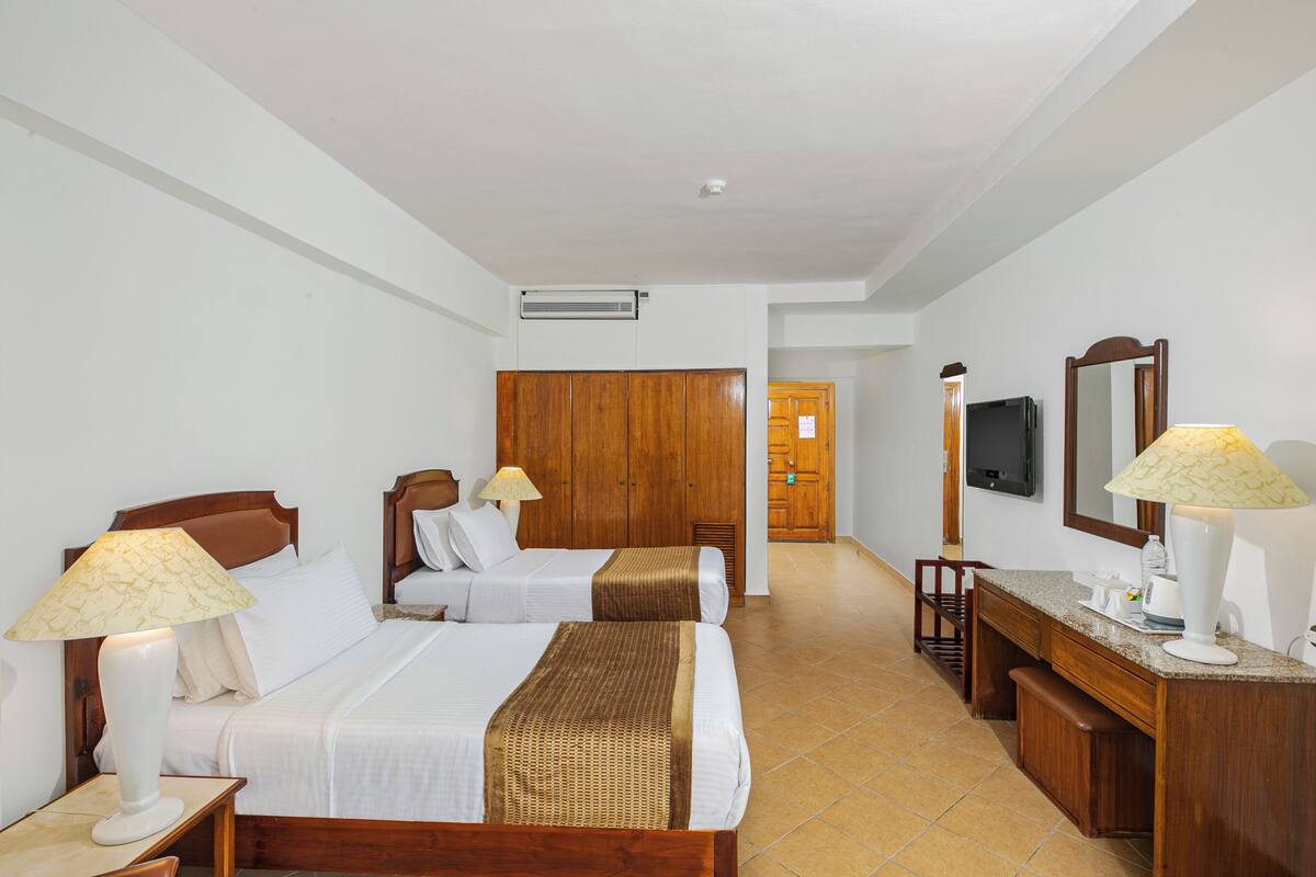 A hotel room with two beds, wooden furniture, a desk, a mirror, and a television.