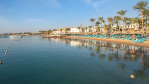A coastal hotel with a beachside view, including a row of palm trees and beach chairs. - Marlin Inn Azur Resort (Hurghada)