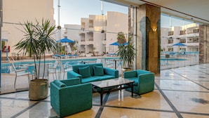 A spacious lobby with a pool area, featuring a seating area with teal sofas and a coffee table, surrounded by potted plants and a glass railing overlooking the pool. - Marlin Inn Azur Resort (Hurghada)
