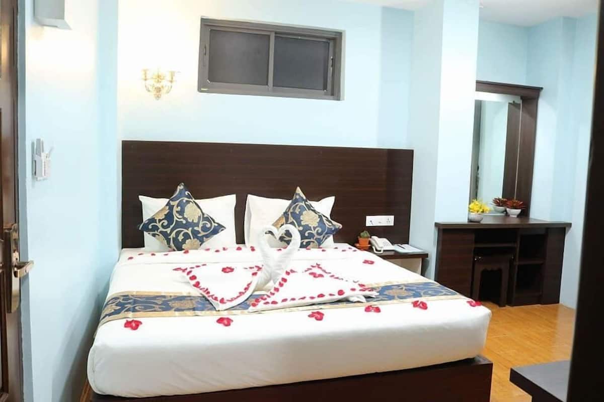 A neatly made bed with a decorative swan and rose petals, a bedside table with a phone, and a small desk with a mirror and plants.