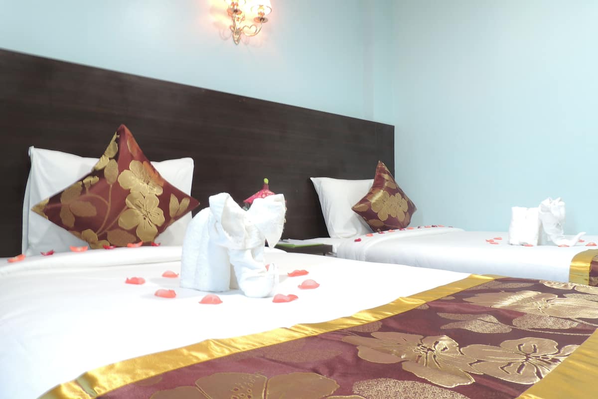 A hotel room with two beds, each with white linens and decorative pillows, a dark headboard, and a wall-mounted light fixture.