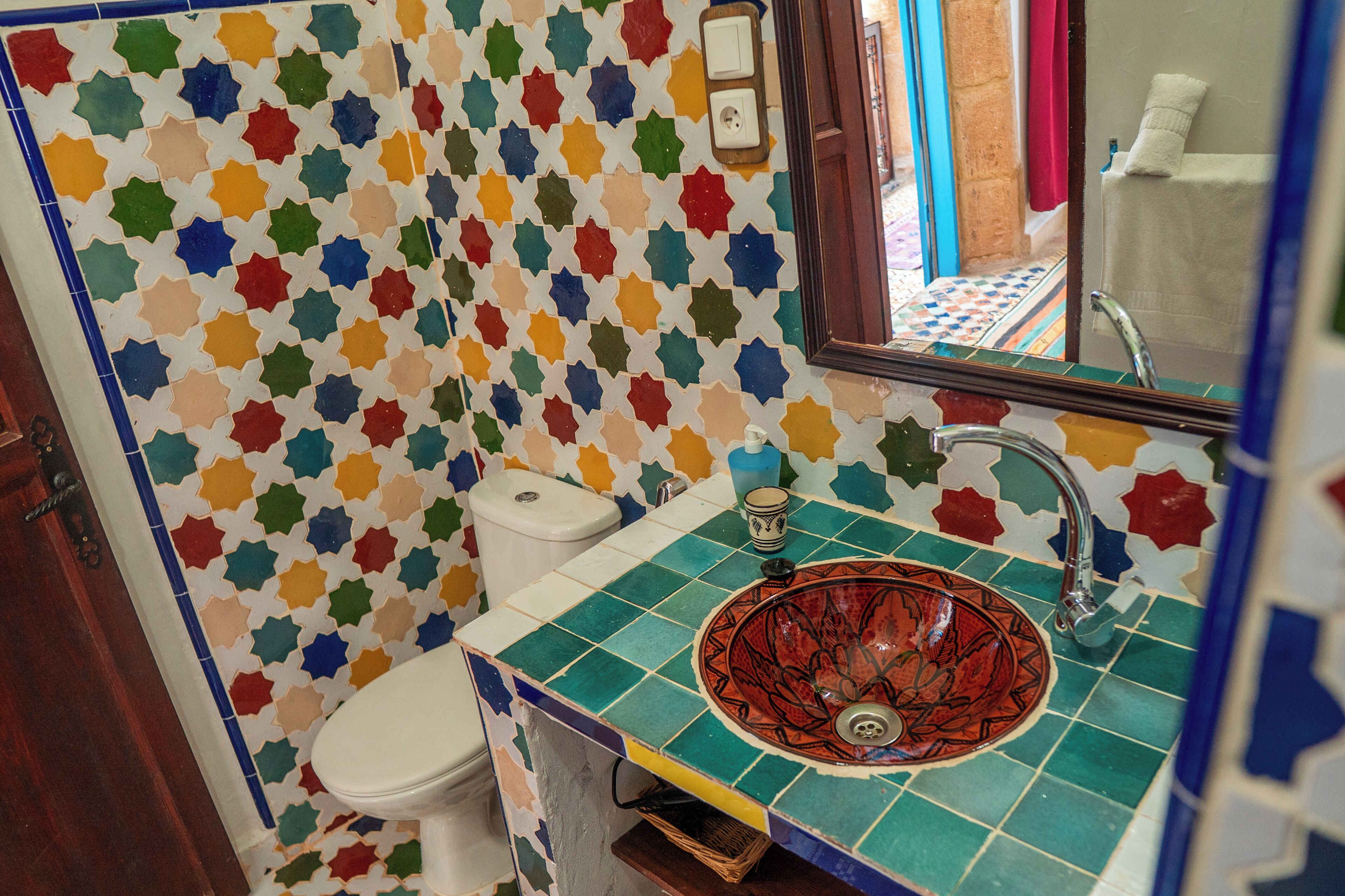 Een badkamer met een kleurrijke wand betegeld met sterrenmotieven, een wit toilet en een rode keramieken wastafel met een enkele kraan.