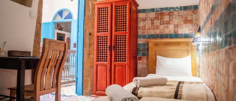 A hotel room with a bed, a wooden chair, a red cabinet, and a view of the outside.