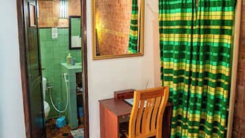 A bathroom with a green tiled floor, a wooden chair, a small table, a mirror, and a green striped shower curtain.