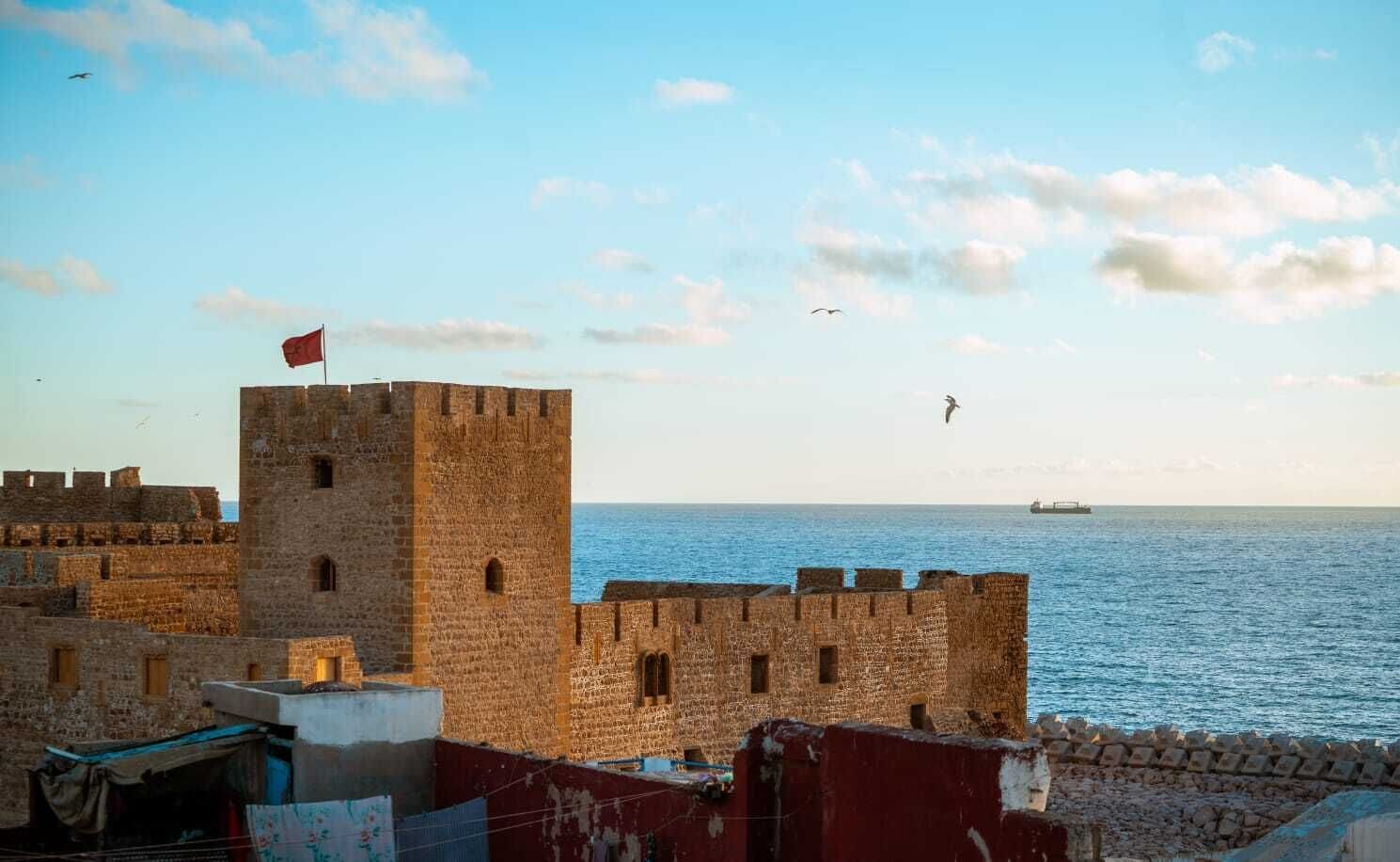 A coastal fortification with a flag, stone walls, and a view of the sea.