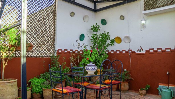 A patio with a table and chairs, potted plants, and a decorative wall. - Riad Le Cheval Blanc (Safi)
