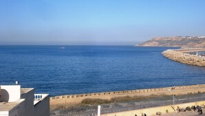 A coastal view with a clear sky, a rocky shoreline, and a distant building on a hill. - Riad Le Cheval Blanc (Safi)