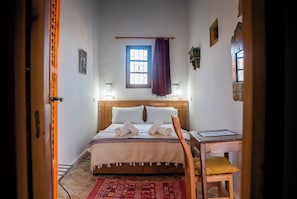Un dormitorio con una cama, una silla, un escritorio, una ventana y una puerta.