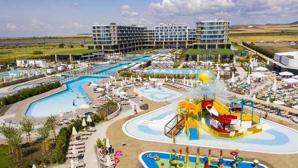 A resort with multiple swimming pools, a water park, and a view of modern buildings in the background.