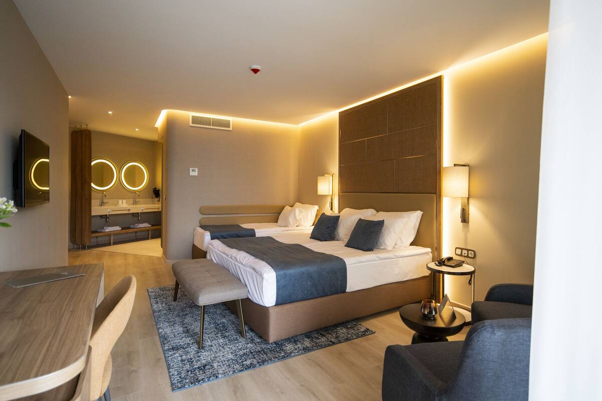 A modern hotel room with a large bed, bedside tables, a desk, and a seating area.