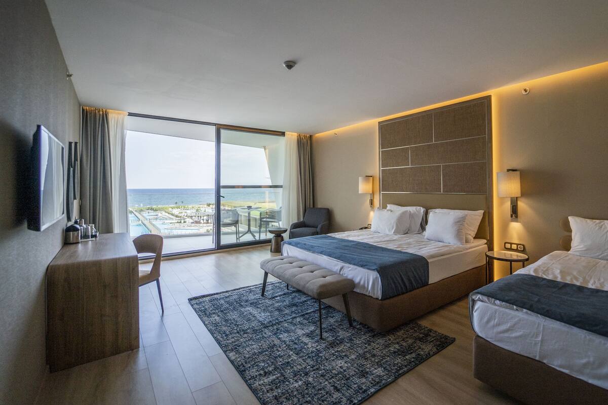 A hotel room with a large bed, a smaller bed, a desk, a chair, and a view of the ocean.