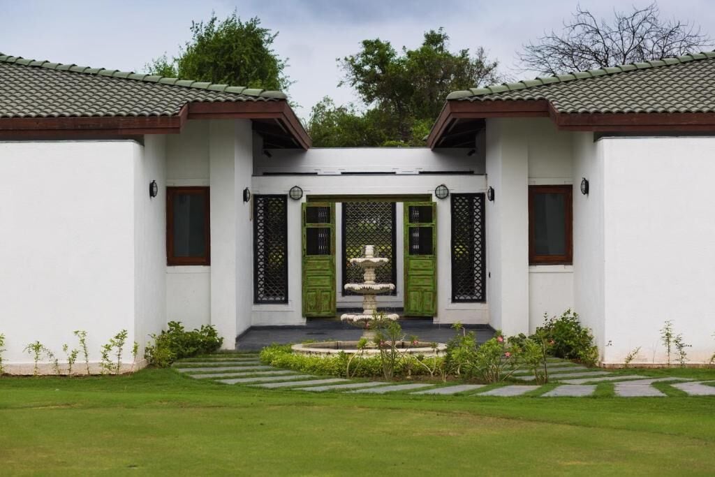 A traditional building with a central fountain, white walls, green doors, and a tiled roof.