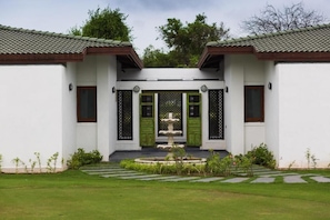 A traditional building with a central fountain, white walls, green doors, and a tiled roof. - Gulmohar Greens - Golf & Country Club (Sanand)