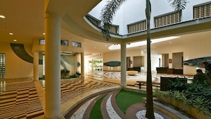 A spacious lobby with a checkered floor, a central seating area, and a staircase leading to upper levels. - Gulmohar Greens - Golf & Country Club (Sanand)
