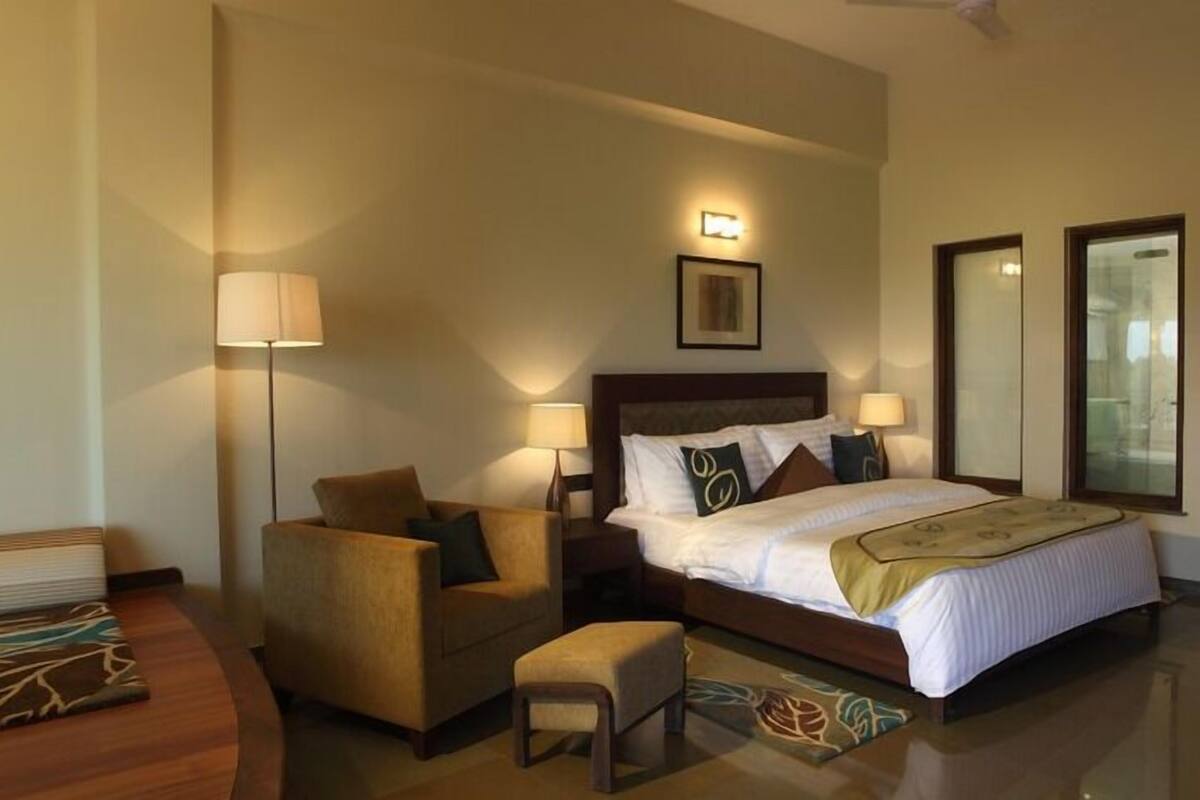 A hotel room with a large bed, a chair, a small table, and a lamp.