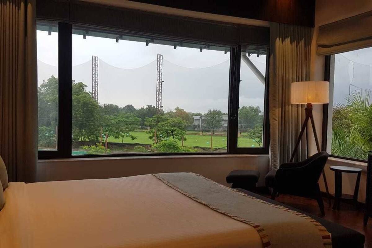 A hotel room with a bed, a desk, and a chair. There is a window with a view of a field and a tower.