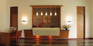 A reception area with a wooden reception desk, a wall-mounted light fixture, and a reception counter. - Gulmohar Greens - Golf & Country Club (Sanand)