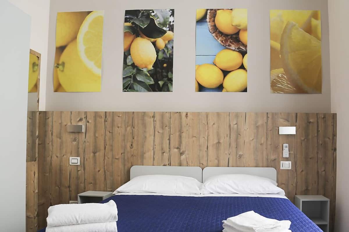 A bedroom with a wooden headboard, a bed with white and blue bedding, and four wall-mounted pictures of lemons.