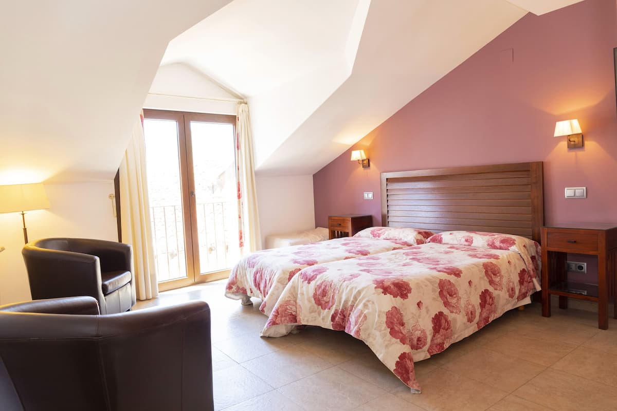 A bedroom with a large bed, two bedside tables, a chair, and a window with curtains.