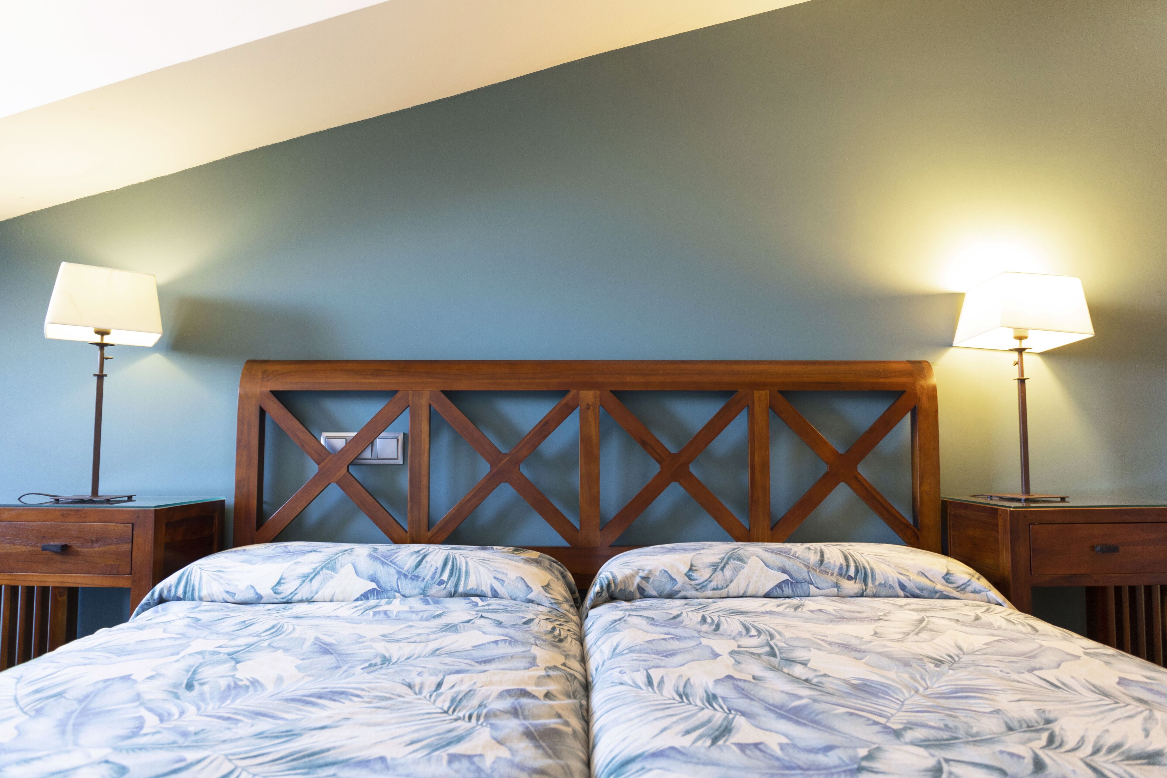 Una cama doble con cabecera de madera y dos mesitas de noche con lámparas.