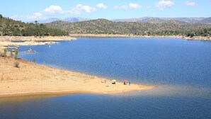 A lake with a sandy beach, a few people, and distant hills. - Casas Rurales Abuela Benita (Cebreros)