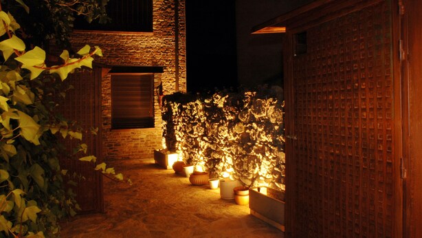 A nighttime view of a courtyard with a brick building, potted plants, and a wooden gate. - Casas Rurales Abuela Benita (Cebreros)