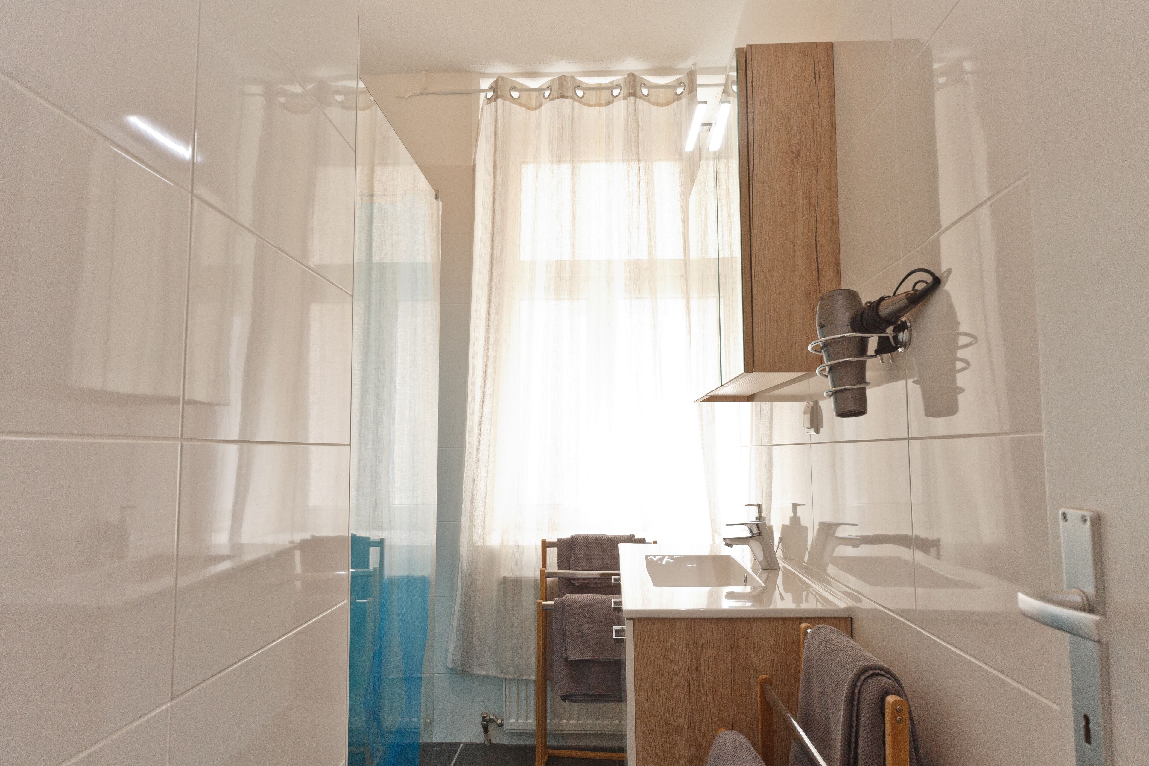 Un baño moderno con cabina de ducha de vidrio, tocador de madera y perchero.