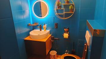 Un baño con un espejo redondo, un lavabo, un inodoro y una estantería con plantas.