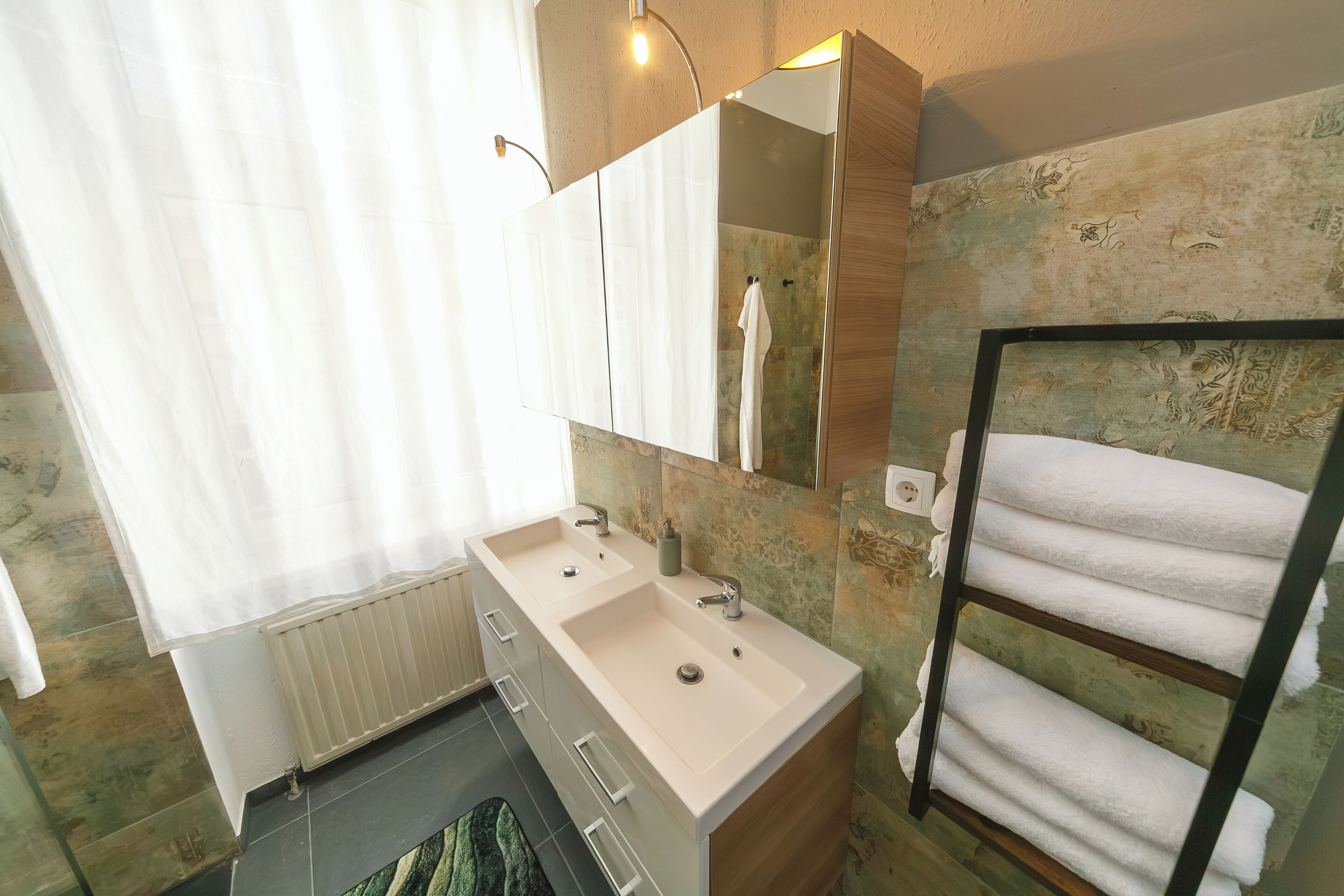 Un baño con lavamanos doble, espejo, toallero y radiador.