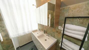 Un baño con lavamanos doble, espejo, toallero y radiador.