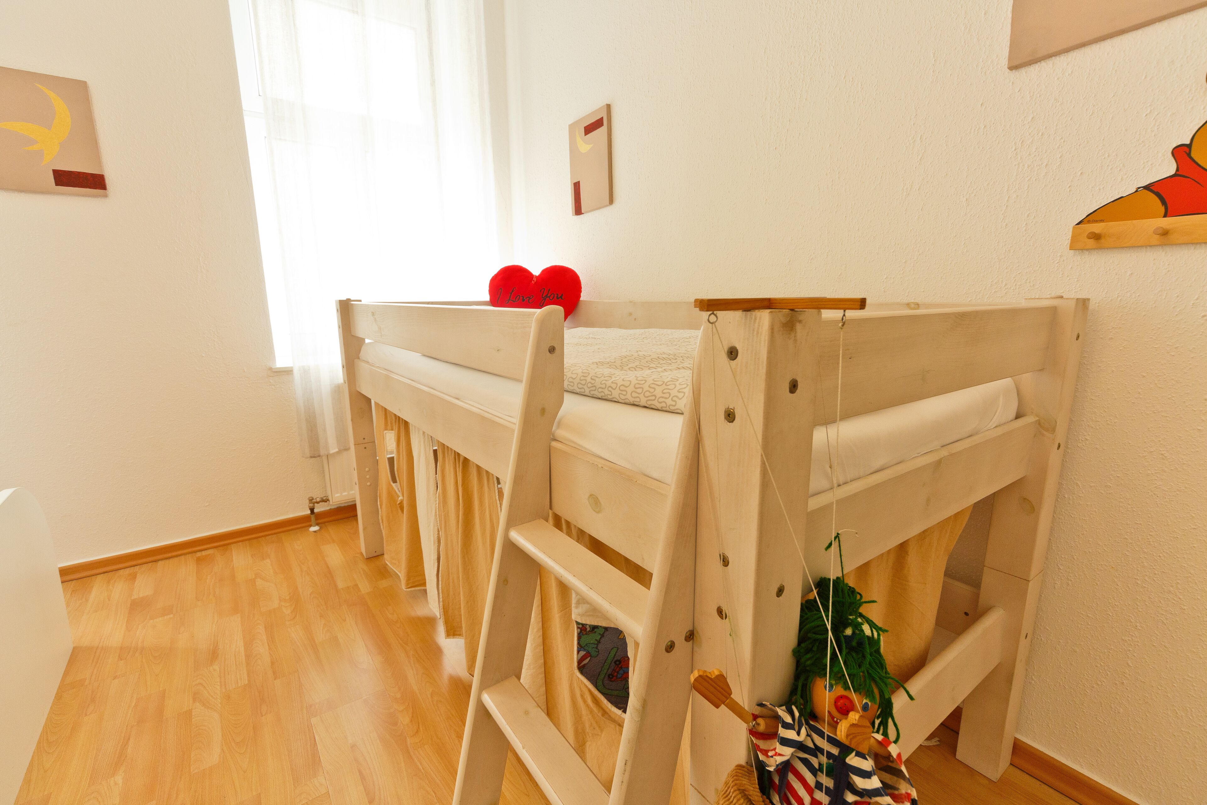 Habitación con literas, una escalera, ventana con cortinas y un cuadro con un estante pequeño en la pared.